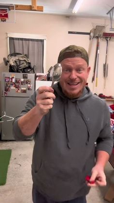 a man holding a spoon in his right hand and looking at the camera while standing in a garage