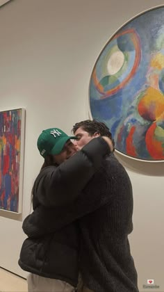 two people hugging each other in front of paintings