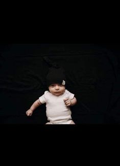 a baby wearing a black hat and white shirt is standing in front of a black background