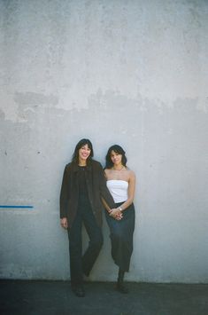 two women standing next to each other in front of a wall