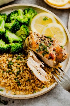 a white plate topped with chicken, rice and broccoli next to lemon wedges