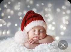 a baby wearing a santa hat laying on top of a white blanket with lights in the background