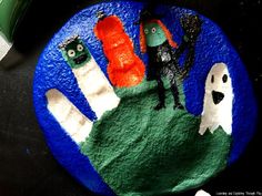 a painted rock with three cartoon figures on it and two ghost hands in the middle