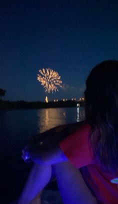 a woman sitting on the back of a boat watching fireworks go off in the sky