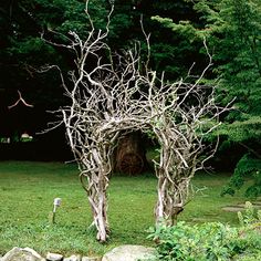 an arch made out of branches in the middle of a field with rocks and grass