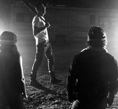 three people standing in the dark with one holding a baseball bat