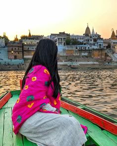 a woman sitting on the back of a boat in front of a lake and buildings