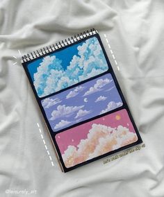 a spiral notebook with three pictures of clouds and the sky on it, sitting on top of a white sheet