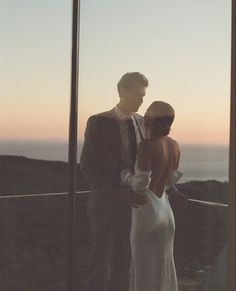 a man and woman standing next to each other in front of a glass wall at sunset