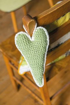 a green crocheted heart hanging from a wooden chair with a pillow on it