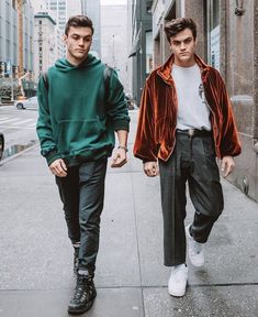 two young men are walking down the sidewalk in front of some tall buildings and one is wearing an orange velvet jacket