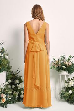 a woman in an orange dress standing next to some flowers and greenery with her back turned towards the camera