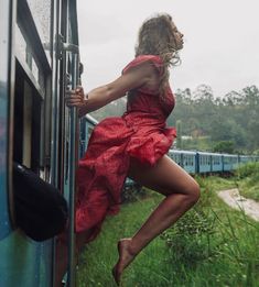 a woman in a red dress leaning on the side of a train