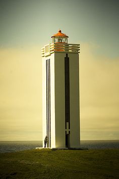 a tall white tower sitting on top of a lush green field next to the ocean