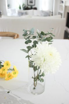 a vase filled with white flowers sitting on top of a table next to a yellow flower