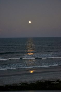 the moon is setting over the ocean with waves