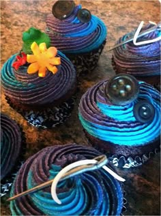 four cupcakes with blue icing and decorations on them sitting on a table