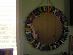 a circular mirror hanging on the wall with books in front of it and a person reaching up to grab one