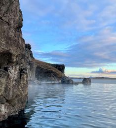 a large body of water surrounded by rocky cliffs and blue sky with clouds in the background