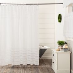 a white shower curtain in a bathroom next to a bathtub and wooden flooring