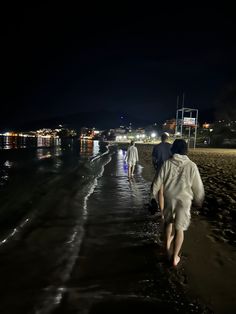 two people walking on the beach at night with their backs turned to the camera as they walk towards the water