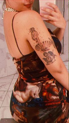 a woman with a tattoo on her arm looking at her cell phone in the mirror