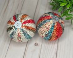 two crocheted balls sitting next to each other on a white wooden floor with green leaves