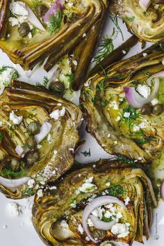 grilled artichokes with herbs and feta cheese on top, served on a white platter