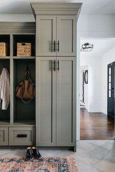 an entryway with gray cabinets and baskets on the floor, shoes hanging in front of it