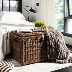 a wicker trunk is sitting on the floor next to a bed with white sheets and pillows