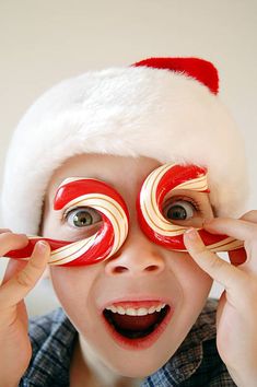 a young boy wearing a santa hat holding candy canes in front of his eyes