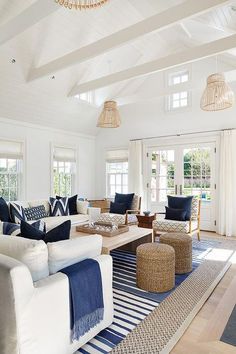 a living room filled with white furniture and blue pillows on top of a wooden table