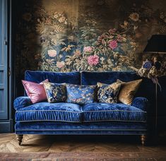 a blue couch with pillows on it in front of a floral wallpaper