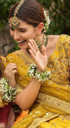 a woman in a yellow sari smiles and holds her hand up to her face