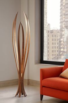 a living room with an orange chair and a tall wooden sculpture in front of a window