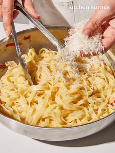 two hands sprinkling parmesan cheese on top of pasta in a pan