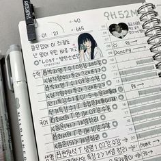 an open notebook with korean characters on it and two pens sitting next to each other