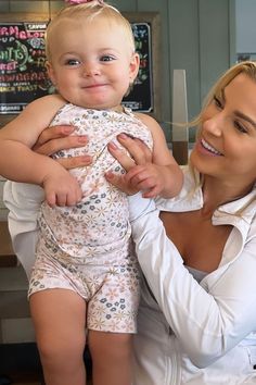 a woman holding a baby in her arms and smiling at the camera while she holds it up