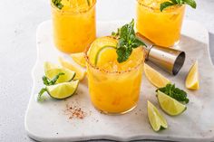 three glasses filled with orange juice and garnished with limes on a white tray