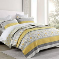 a bed with yellow and gray bedspread in a bedroom next to a window