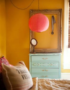 a bedroom with yellow walls and a blue dresser next to a mirror on the wall