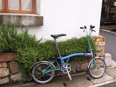 a blue and green bike parked next to a stone planter on the side of a building