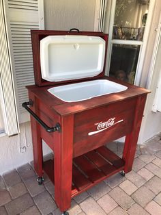 an old coca - cola cooler is sitting outside on wheels