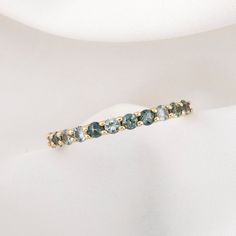 a gold ring with blue and green stones on it's side sitting on a white cloth