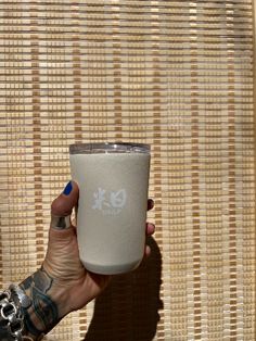 a person holding a cup in front of a bamboo wall with the shadow of their hand on it