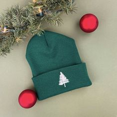 a green beanie hat with a white christmas tree on it next to red ornaments