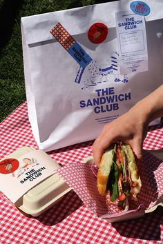 a sandwich is being held up by someone at a picnic table with an ice cream box