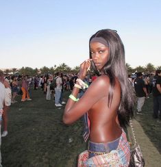 a woman standing in the grass talking on a cell phone with people behind her watching