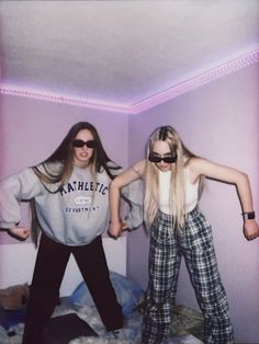 two people standing on top of a bed in a room with purple lighting and one person wearing sunglasses