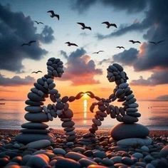 two hearts made out of rocks on the beach with seagulls flying in the background